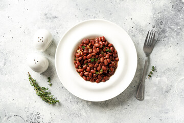 Stewed red beans with onion and thyme in tomato sauce in a white plate on the kitchen table top view