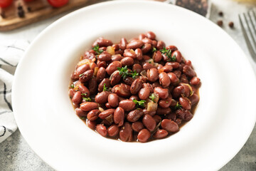 Stewed red beans with onion and thyme in tomato sauce in a white plate on the kitchen table closeup
