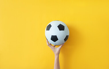 Female hand holding soccer ball on yellow background