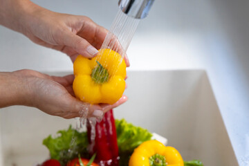 Woman washing vegetables on kitchen counter.