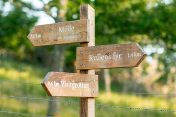 Trail sign on a hiking trail in Kullabergs naturreservat, Skåne, Sweden. Kullens fyr is in focus, the old lighthouse on the tip of the peninsula. Mölle and visitgrottan out of focus in the other way
