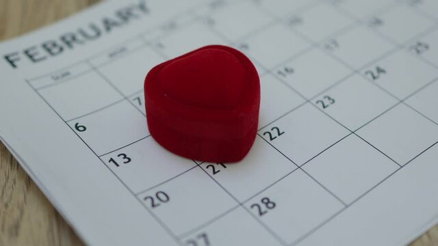 hand putting heart shape red ring box on paper month planner calendar February 14 date. Valentine's Day celebrating holiday love concept, jewelry gift present surprise on valentine engagement proposal