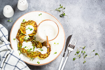 Zucchini pancakes with spinach, hepbs and parmesan cheese, served with sour cream or yogurt. Top view at stone table.