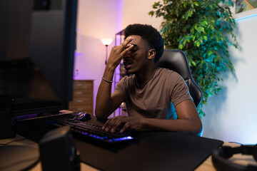 Professional pro video gamer playing on computer lost round in the game, he is heartbroken, disappointed, ashamed, the man covers face with hand, the room lit with led neon lights © ABCreative