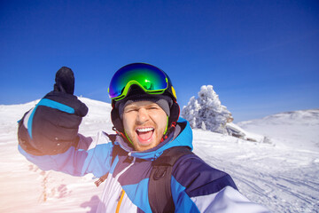 Fototapeta na wymiar Winter recreation on nature ski tour, smile man skier makes selfie photo on background of snowy forest in mountains sunny
