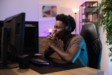 Disappointed sad angry gamer loses game, hands joined covers face, has headset, looks at monitor sadly, room lit with blue and purple led lights © ABCreative
