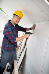 drywall worker with yellow safety helmet works on building site in a house