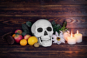 Human skull with flowers, fruits and two burning candles on wooden surface. Apples, tangerines, fir...