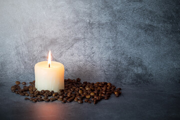 Burning candle among scattered coffee beans on gray background