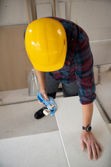 drywall worker with yellow safety helmet works on building site in a house - obrazy, fototapety, plakaty