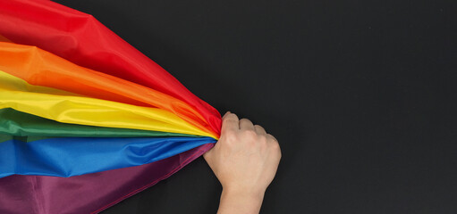 Hand is holding rainbow flag on black background.