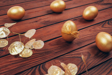 Golden colored Easter eggs with dry flowers over dark wooden planked background.