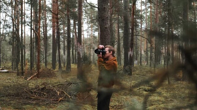 A young blond male photographer takes pictures of nature. Photographer takes pictures in the woods in the winter couple. Young photographer. . High quality 4k footage