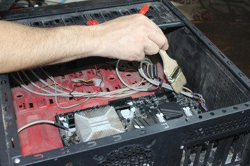A man cleans a computer from dust with a brush, a close-up of a dirty system unit of a personal computer