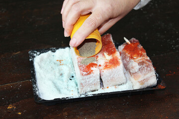 Close-up of a caucasian elderly woman's hand peppers fat. Salo with garlic, allspice, paprika and seasoning for lard