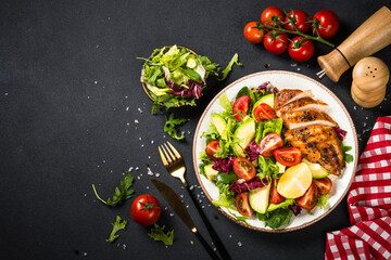 Healthy chicken salad with leaves, vegetables and Grilled chicken steak. Top view at black table.