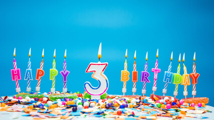 Happy birthday candle letters with number three on a beautiful blue background. Copy space Happy birthday greetings for 3 years old child, lit candles with holiday decorations