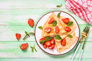 Crepes with fresh srawberries and honey. Summer dessert or breakfast. Top view at wooden table.
