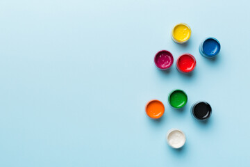 jars with gouache of different colors on Colored background. hobby painting. Top view with empty...