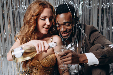 Interracial couple in love celebrating. African man and Caucasian woman having fun and drinking champagne.