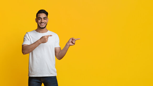 Cheerful middle eastern guy pointing at copy space