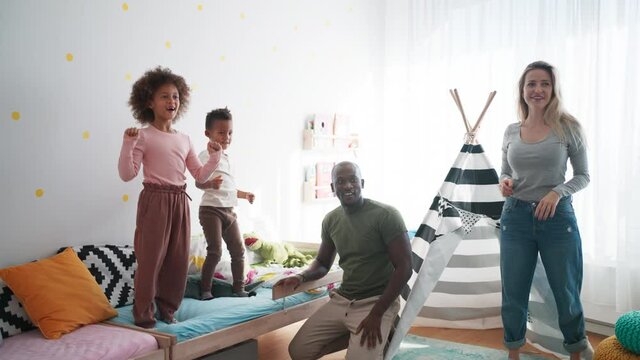 Two little multiracial kids with mother and father playing with toy planes at home.