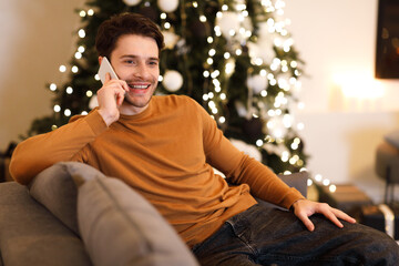Cheerful man talking on cellphone sitting on couch