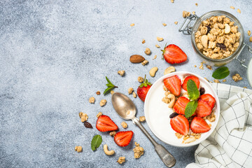 Yogurt with granola and strawberry in white bowl at stone table. Top view with copy space.