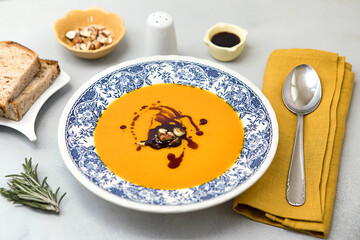 Fresh pumpkin cream soup on the plate with hazelnuts and pumpkin oil, served with fresh bread.  Ready to eat butternut squash soup on neutral background. Vegan food.