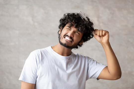 Dry And Matted Hair. Indian Young Guy In White T-shirt Combining With Brush And Having Pain From Tangled Curly Hair