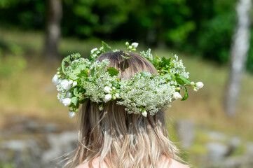 Woman with a flower wreath on her head. Midsummer celebration, a Swedish feast and tradition in June. Photography taken from behind, blurred bokeh background, copy space, place for text.