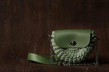 Crocheted green clutch bag on a silver chain on a dark brown background