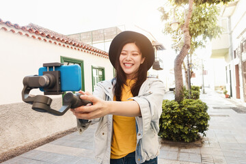 Happy asian influencer girl having fun vlogging with gimbal and mobile phone outdoor - Focus on face
