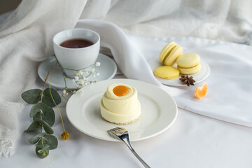 Minimalistic mini cake with white and yellow glaze and cup of tea on the table