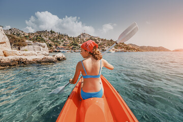 Happy girl is rowing on a sea kayak near Kekova island with view of Simena Castle and Kaleucagiz village in Turkey. Outdoor recreation and exploration. Travel as a lifestyle