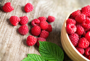 Fresh ripe red raspberries with leaves in a bowl on rustic old wooden table. Healthy organic food, summer vitamins, BIO viands, natural background. Copy space for your advertising text message.