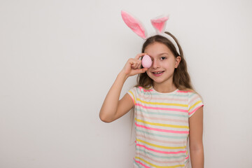 Portrait of smiling brunette girl in bunny ears holding pink easter egg in her hand and looking at camera, happy easter