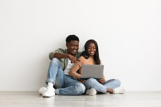 Happy black couple sitting on floor with laptop, having conversation