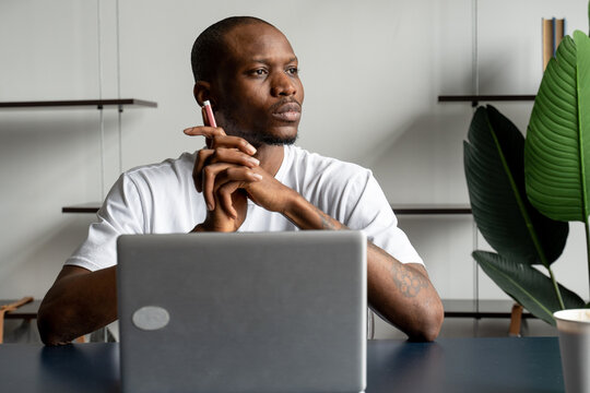 Thoughtful black businessman sitting at a desk with a computer and looking away. Distracted from his studies, the young man plunged into thought