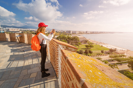 Happy tourist woman taking picture while stands on the White Tower viewpoint and enjoys the panorama of Thessaloniki city in Greece