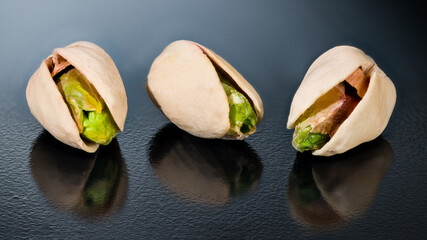 Closeup of salty roasted pistachio nuts cores with reflection on shiny black background. Pistacia...