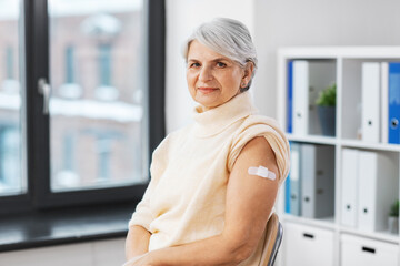 medicine, health and vaccination concept - vaccinated senior woman with medical patch on arm at...