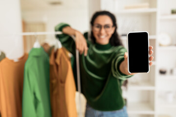 Unrecognizable Woman Showing Smartphone Screen Standing Near Clothing Rail Indoors