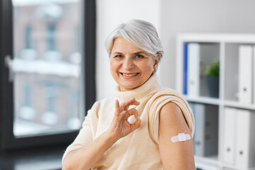 medicine, health and vaccination concept - happy smiling vaccinated senior woman with medical patch...