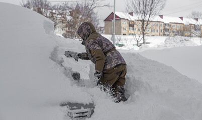 a man digs his car out of the snow captivity.car covered with snow after a heavy snow storm