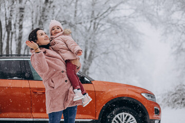Mother with little daughter in a winter park by car