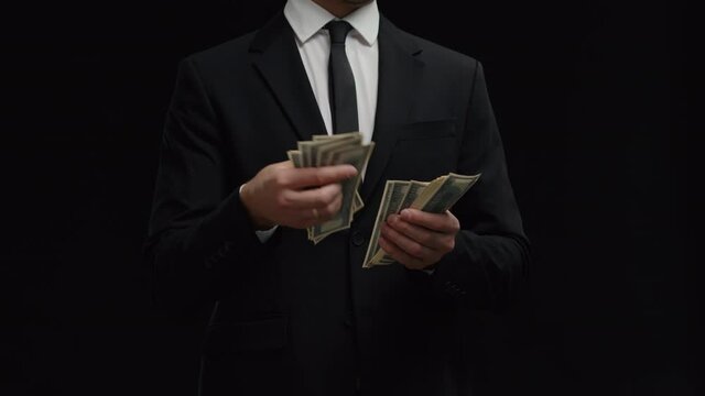 Unrecognized incognito man financial adviser holding and counts money banknotes wear black suit. Management shady business. Shadow Investor counting profit of dollar bills cash.