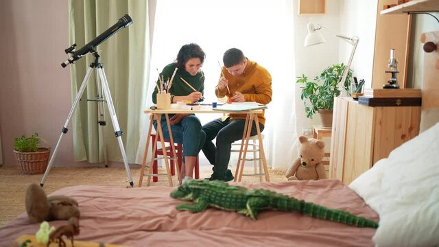 Young man with Down syndrome with his tutor painting pictures indoors at home, homeschooling.
