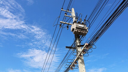 Transformer on the pole. Three-phase AC high voltage transformer with high and low voltage transmission line on concrete pole on blue sky white cloud background with copy space. Selective focus