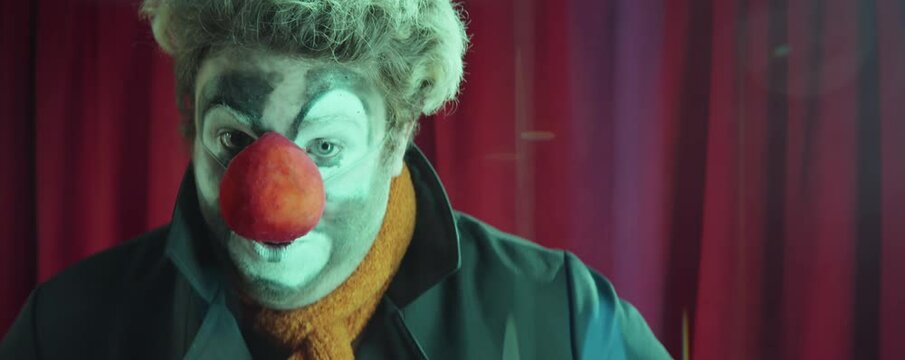 Portrait of funny clown with makeup and red sponge nose making faces on camera while performing on stage